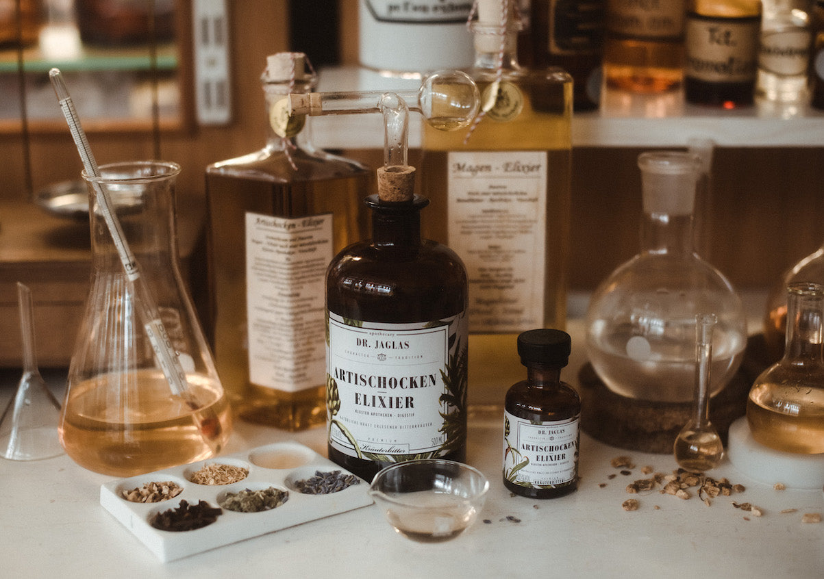 Dr Jaglas Artischocken Elixier- in großer und kleiner Flasche und verschiedenen Kräuterkomponenten